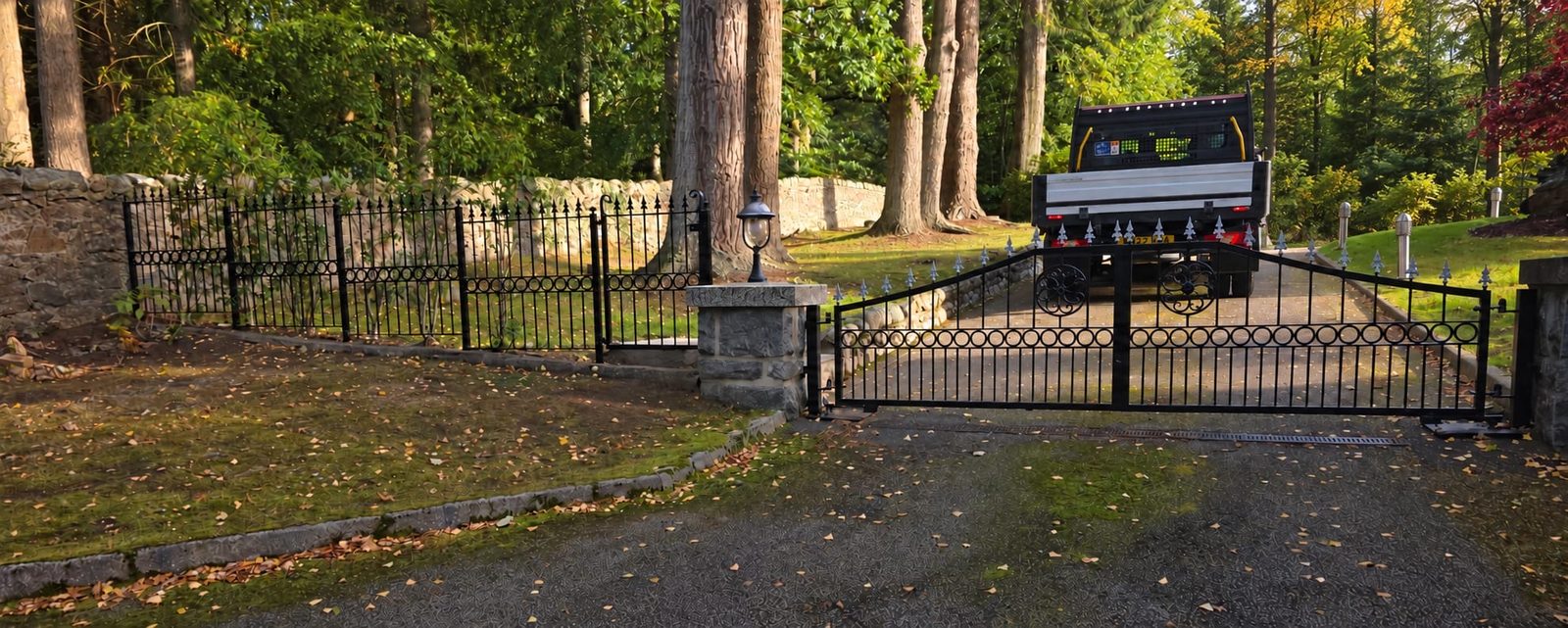 Black steel arched double driveway gates with matching railings and side gate at a stone pillar entrance